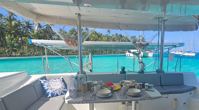 Mesa de desayuno en la cubierta de un catamarán con aguas turquesas y una isla de San Blas al fondo